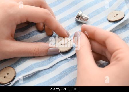 Frau näht Knopf auf gestreiftem Hemd, Nahaufnahme Stockfoto