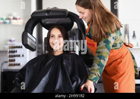 Junge Dame unter der Frisiermaschine, während sie in den Spiegel schaute Stockfoto