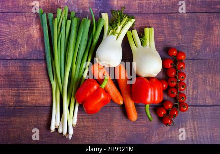 Frische Frühlingszwiebeln, Fenchel, Karotten, Tomaten und Paprika auf einem rustikalen Holztisch. Gesunde Zutaten für die Hausmannskost zur Unterstützung des Immunsystems. Stockfoto