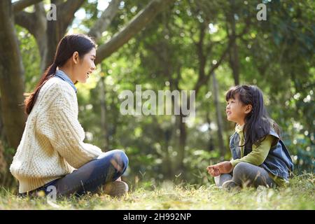 Junge asiatische Mutter und Tochter genießen ein Gespräch im Stadtpark Stockfoto