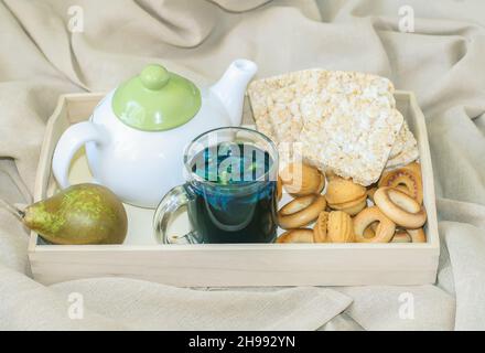 Frühstück im Bett in einem Holztablett mit Birne, Bisquits, süßen Plätzchen, Teekannen und einer Tasse Bio-blauen thailand-Tee Anchan, clitoria, Schmetterlingserbse. Stockfoto
