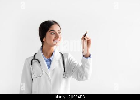 Fröhliche tausendjährige hindu-Frauentherapeutin im Mantel schreibt mit Stift auf leeren Raum Stockfoto