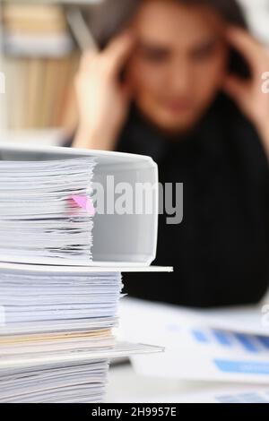 Müde und erschöpfte Frau schaut auf Dokumente und berührt den Kopf mit den Händen Stockfoto