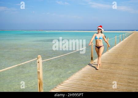 Lächelnde junge Frau im weihnachtshut, die auf einem hölzernen Ponton läuft Stockfoto
