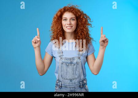 Motiviert glücklich fröhlich rothaarig albern lockig Frau zeigt nach oben inrdex Finger lächelnd verzaubert beeindruckt aufgeregt zeigt genial promo diskutieren Stockfoto
