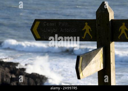 Fußpfadschild am Küstenpfad in Wales mit Wellen an felsiger Küste unten Stockfoto