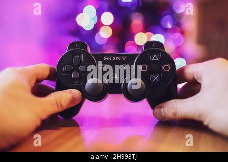 5th. Dezember 2021, Cork, Irland - Ein schwarzer Sony PlayStation 3-Controller wird von einem Erwachsenen mit einem unscharfem weihnachtsbaum im Hintergrund gehalten; g Stockfoto