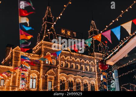 Goldenes Gebäude, das mit magischen Lichtern am Abend, geschmückt mit festlichen Girlanden und Fahnen, brennt. Neujahr und Weihnachtsstimmung in Moskau Stockfoto