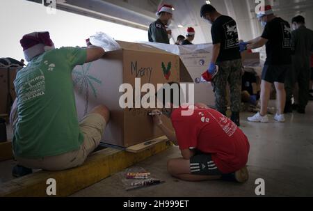 Yigo, Usa. 04th Dez 2021. Freiwillige packen gespendete Güter und schmücken Lufttropfenbündel mit Botschaften zur Unterstützung der jährlichen Operation Christmas Drop 70th auf der Andersen Air Force Base am 4. Dezember 2021 in Yigo, Guam. Jedes Jahr im Dezember werden die Luftbesatzungen 55 Inselnationen im gesamten Südost-Pazifik Nahrungsmittel, Vorräte, Unterrichtsmaterialien und Werkzeuge von AirDrop spenden. Kredit: 1lt. Jade Watkins/US Airforce Foto/Alamy Live News Stockfoto