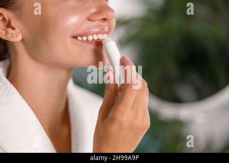Nahaufnahme einer lächelnden Frau, die Lippenbalsam anwendet und sich um ihre Lippen kümmert Stockfoto