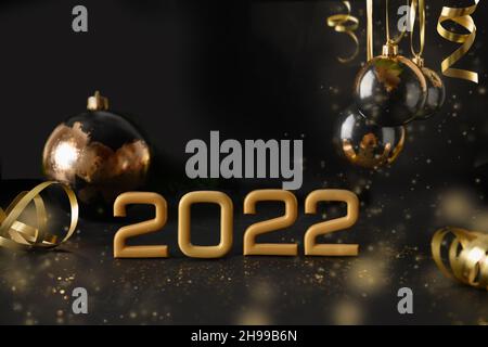Neujahr 2022 Komposition mit Jahreszahl, festlichen schwarzen und goldenen Kugeln, Weihnachtsschmuck auf schwarzem Hintergrund. Grußkarte zum frohen Neujahr Stockfoto