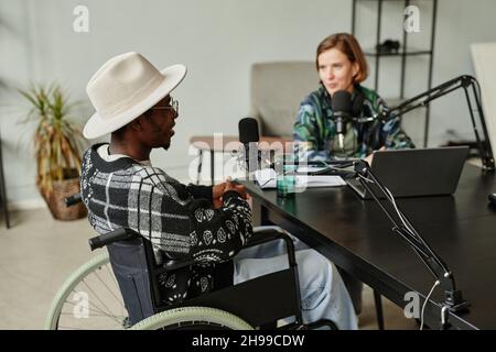Portrait einer jungen weiblichen Schöpferin, die eine Person mit Behinderung interviewt, während sie Podcast aufzeichnet Stockfoto