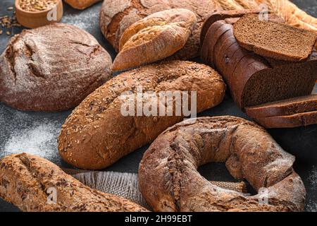 Roggen- und Weizenbrot auf dunklem Grund mit Mehl. Seitenansicht, Nahaufnahme. Stockfoto