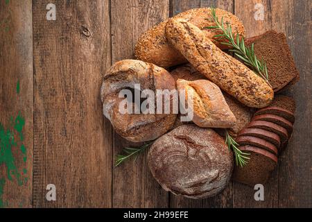 Verschiedene Brotsorten mit frischem Rosmarin auf Holzboden. Draufsicht, Kopierbereich. Stockfoto