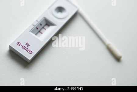 Rapid Antigen Detection Test (RADT) mit COVID-19 AG-Inschrift und zwei roten Streifen, die ein POSITIVES Ergebnis eines auf dem liegenden menschlichen Probentests zeigen Stockfoto