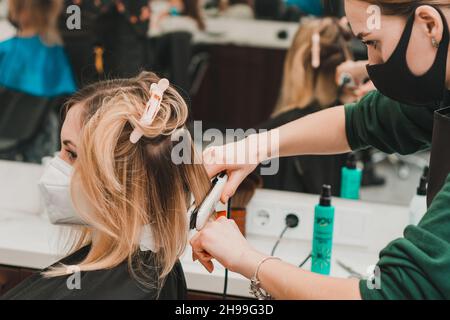 Dolyna, Ivano-Frankivsk 5. März 2021: Haarglättung in einem Friseursalon, Stylist arbeitet in Quarantäne, Arbeit in medizinischen Masken. Stockfoto