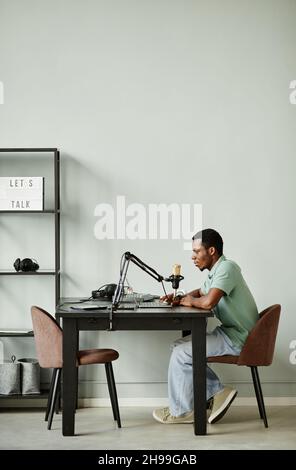Seitenansicht in voller Länge: Porträt eines afroamerikanischen Mannes, der mit der Kamera spricht, während er zu Hause Podcast aufzeichnet Stockfoto