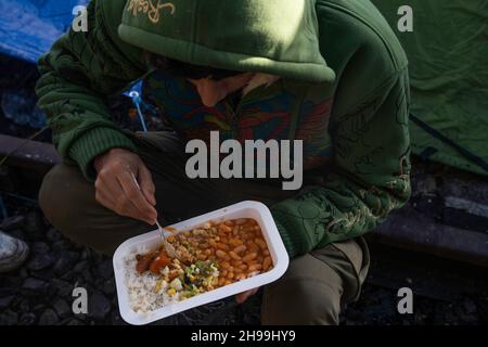 Dünkirchen, Frankreich. 05th Dez 2021. Ein Migrant, der von einer NGO in einem provisorischen Migrantenlager zu Mittag gegessen wird.Schätzungen zufolge leben derzeit etwa 800 Migranten/Flüchtlinge in der Region Dünkirchen in Nordfrankreich. Die meisten von ihnen warten auf ihre Möglichkeiten, entweder mit einem aufblasbaren Schlauchboot nach Großbritannien zu kommen oder sich in Lastwagen zu verstecken. Kredit: SOPA Images Limited/Alamy Live Nachrichten Stockfoto