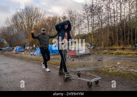 Dünkirchen, Frankreich. 05th Dez 2021. Migranten sehen, wie sie einen Supermarktwagen in ein provisorisches Migrantenlager schieben.Schätzungen zufolge leben derzeit rund 800 Migranten/Flüchtlinge in der Region Dünkirchen in Nordfrankreich. Die meisten von ihnen warten auf ihre Möglichkeiten, entweder mit einem aufblasbaren Schlauchboot nach Großbritannien zu kommen oder sich in Lastwagen zu verstecken. Kredit: SOPA Images Limited/Alamy Live Nachrichten Stockfoto