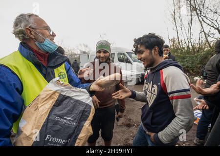 Dünkirchen, Frankreich. 05th Dez 2021. Ein Freiwilliger einer NGO sah, wie er Brot an Migranten in einem provisorischen Migrantenlager verteilte.Schätzungen zufolge leben derzeit etwa 800 Migranten/Flüchtlinge in der Region Dünkirchen in Nordfrankreich. Die meisten von ihnen warten auf ihre Möglichkeiten, entweder mit einem aufblasbaren Schlauchboot nach Großbritannien zu kommen oder sich in Lastwagen zu verstecken. Kredit: SOPA Images Limited/Alamy Live Nachrichten Stockfoto