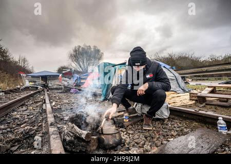 Dünkirchen, Frankreich. 05th Dez 2021. Ein Migrant aus der kurdischen Region des Irak sah in einem provisorischen Migrantenlager kochendes heißes Wasser, um Tee zuzubereiten.Schätzungen zufolge leben derzeit etwa 800 Migranten/Flüchtlinge im nordfranzösischen Dünkirchen. Die meisten von ihnen warten auf ihre Möglichkeiten, entweder mit einem aufblasbaren Schlauchboot nach Großbritannien zu kommen oder sich in Lastwagen zu verstecken. Kredit: SOPA Images Limited/Alamy Live Nachrichten Stockfoto