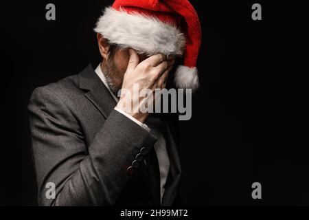 Sehr trauriger Geschäftsmann mit Weihnachtsmannhut weint mit Händen, die das Gesicht bedecken, ein dezernes Porträt mit selektivem Fokus Stockfoto