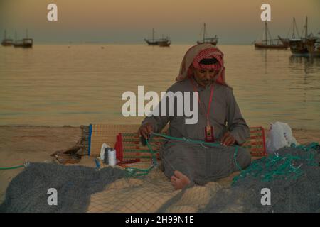 Ein traditioneller arabischer Handwerker webt Fischnetz im Katara Kulturdorf, Doha Katar Tageslichtansicht mit Daus im arabischen Golf im Hintergrund Stockfoto