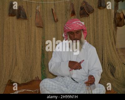 Ein traditioneller arabischer Handwerker webt Fischnetz im Katara Kulturdorf, Doha Katar Tageslichtansicht mit Daus im arabischen Golf im Hintergrund Stockfoto
