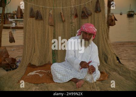 Ein traditioneller arabischer Handwerker webt Fischnetz im Katara Kulturdorf, Doha Katar Tageslichtansicht mit Daus im arabischen Golf im Hintergrund Stockfoto