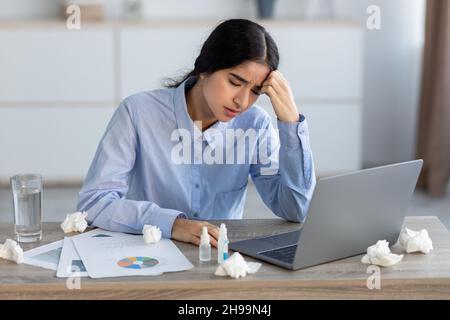 Verzweifelte junge hindu-Managerin krank, drückt Hand an Kopf, leidet unter Kopfschmerzen, Kälte und Schmerzen im Büro Stockfoto