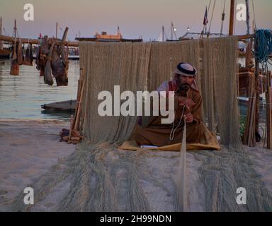 Ein traditioneller arabischer Handwerker webt Fischnetz im Katara Kulturdorf, Doha Katar Tageslichtansicht mit Daus im arabischen Golf im Hintergrund Stockfoto