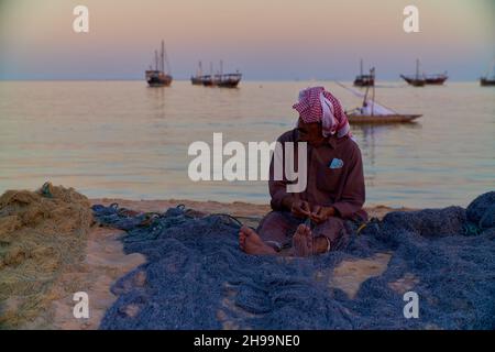 Ein traditioneller arabischer Handwerker webt Fischnetz im Katara Kulturdorf, Doha Katar Tageslichtansicht mit Daus im arabischen Golf im Hintergrund Stockfoto