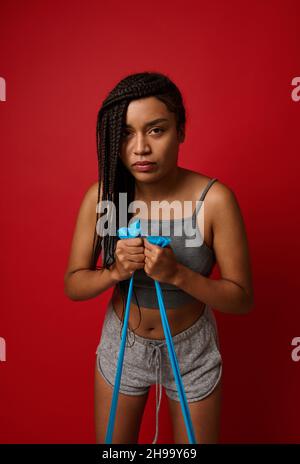 Eine starke junge afrikanische Frau mit stilvollen Dreadlocks, die ein Widerstandsband in ihrer Trainingsroutine verwendet. Athletinnen trainieren mit Widerstandsband aga Stockfoto