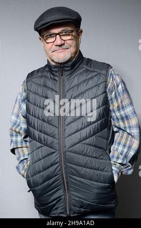 Ein älterer Mann in einer Daunenweste mit Brille und Mütze auf einem neutralen, halblangen Porträt Stockfoto