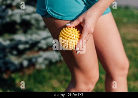 Spiky Gummi-Massage-Ball in den Händen der jungen Frau in Shorts für Cellulite-Reduktion und Gewichtsverlust auf Rasen im Garten am Sommermorgen Stockfoto