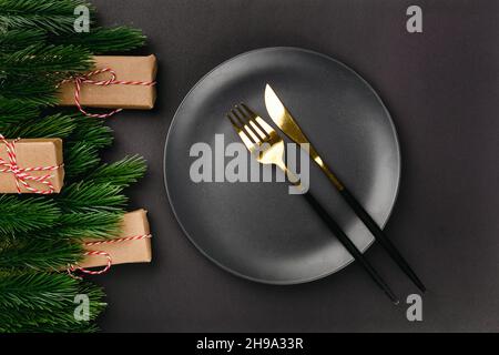 Flaches Lay serviert mit festlichen Gerichten schwarzer Weihnachtstisch mit Rahmen von Dekorationen aus Fichtenzweigen und Geschenken in Bastelpapier Stockfoto