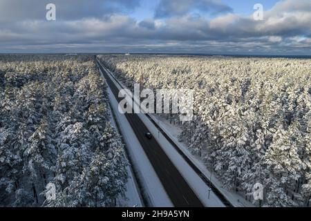 Luftaufnahme der Asphaltstraße, die durch frostige Winterwälder und mit Reif und Schnee bedeckte Haine führt. Drohnenfoto von schwarzer Straßenlinie und Bäumen mit kühlem Schnee in den Bergen. Weihnachtsthema Stockfoto