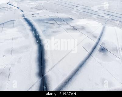 Luftdrohne Draufsicht auf schneebedeckten gefrorenen See oder Fluss Oberfläche mit großen rissigen Eis diagonalen Linien. Natürliche Winterlandschaft abstrakte Textur Stockfoto