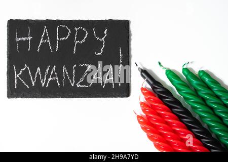 Happy Kwanzaa Konzept. Afro-amerikanischer Feiertag. Gratulationsschriftzug und sieben Kerzen - rot, schwarz und grün. Afrikanisches Erbes-Symbol auf einer weißen BA Stockfoto