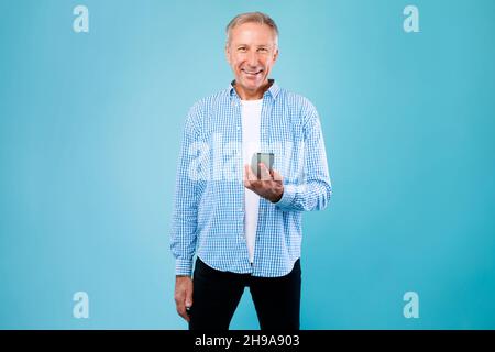 Glücklicher reifer Mann, der sein Mobiltelefon im Blue Studio benutzt Stockfoto