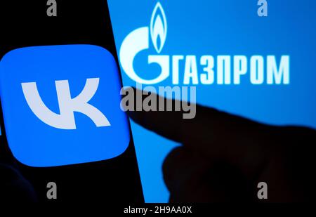 Das Logo der VK-App auf einem Smartphone und DAS GAZPROM-Logo auf dem verschwommenen Laptop. Wort auf russisch übersetzt als „GAZPROM“. Konzept. Stafford, Vereinigtes Königreich, De Stockfoto