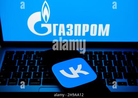 Das Logo der VK-App auf einem Smartphone und DAS GAZPROM-Logo auf dem verschwommenen Laptop. Wort auf russisch übersetzt als „GAZPROM“. Konzept. Stafford, Vereinigtes Königreich, De Stockfoto