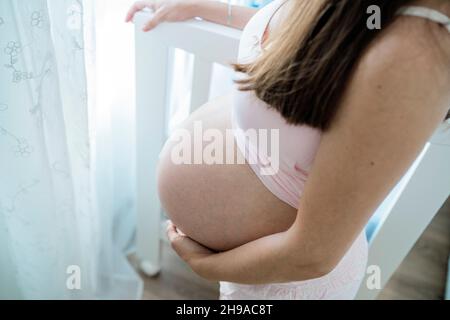 Nicht erkennbare Schwangere, die im Babyzimmer den Bauch berührt Stockfoto