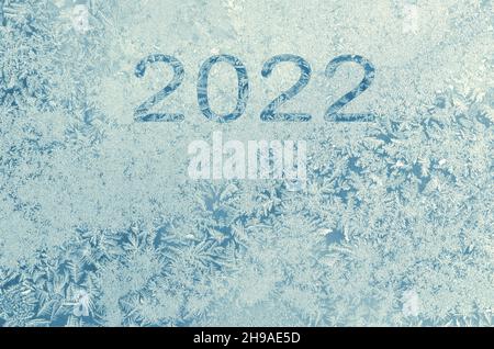 Inschrift über das neue Jahr 2022 auf den frostigen Mustern auf dem Fensterglas in der Wintersaison als hellblauer Hintergrund mit Kopierfläche. Glücklich Stockfoto