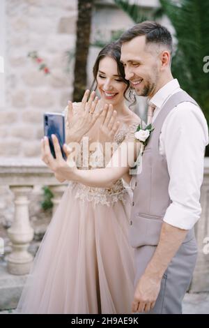 Braut und Bräutigam machen ein Selfie mit Ringen an den Fingern auf einem Smartphone Stockfoto