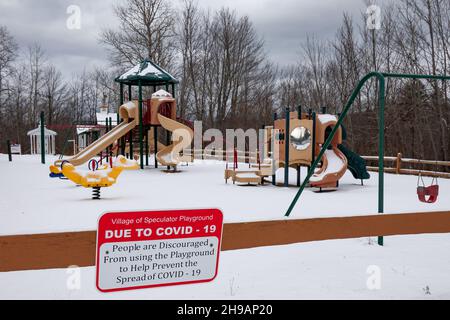 Ein leerer, schneebedeckter Spielplatz in Speculator, NY, USA mit einem COVID-19 Warnschild, das den Einsatz verhindert. Stockfoto