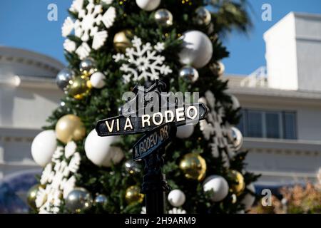 Nahaufnahme des Straßenschildes an der berühmten Kreuzung von Rodeo Drive und Via Rodeo mit dem Weihnachtsbaum im Hintergrund Stockfoto