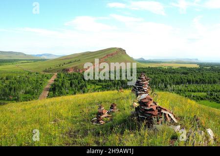 Eine Gruppe von kleinen Steinpyramiden auf einem Hügel mit Blick auf die endlose Steppe und die Bergkette. Truhen, Chakassien, Sibirien, Russland. Stockfoto