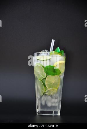 Mojito, starker Alkohol in einem hohen Glas mit Eis, Minze und Limette auf schwarzem Hintergrund. Vertikale Positionierung. Stockfoto