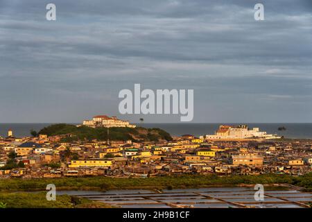 Blick auf die Stadt von Elmina bei Sonnenuntergang mit der Burg von Elmina (St. George's Castle/Fort Saint Jorge), UNESCO-Weltkulturerbe, auf der rechten Seite, Fort Coenraadsburg Stockfoto